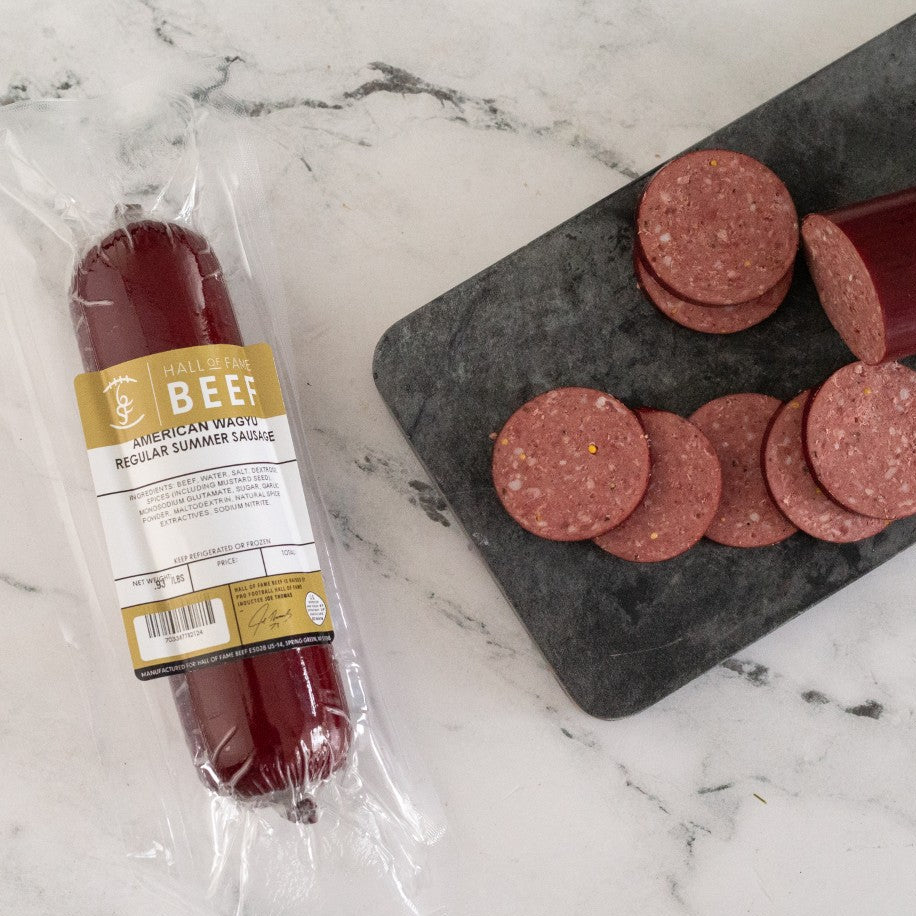 Packaged beef sausage on a marble surface with sliced links on a cutting board.
